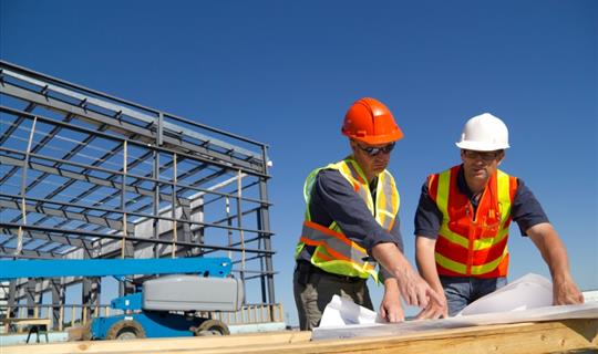 two men on a building site looking at construction plans